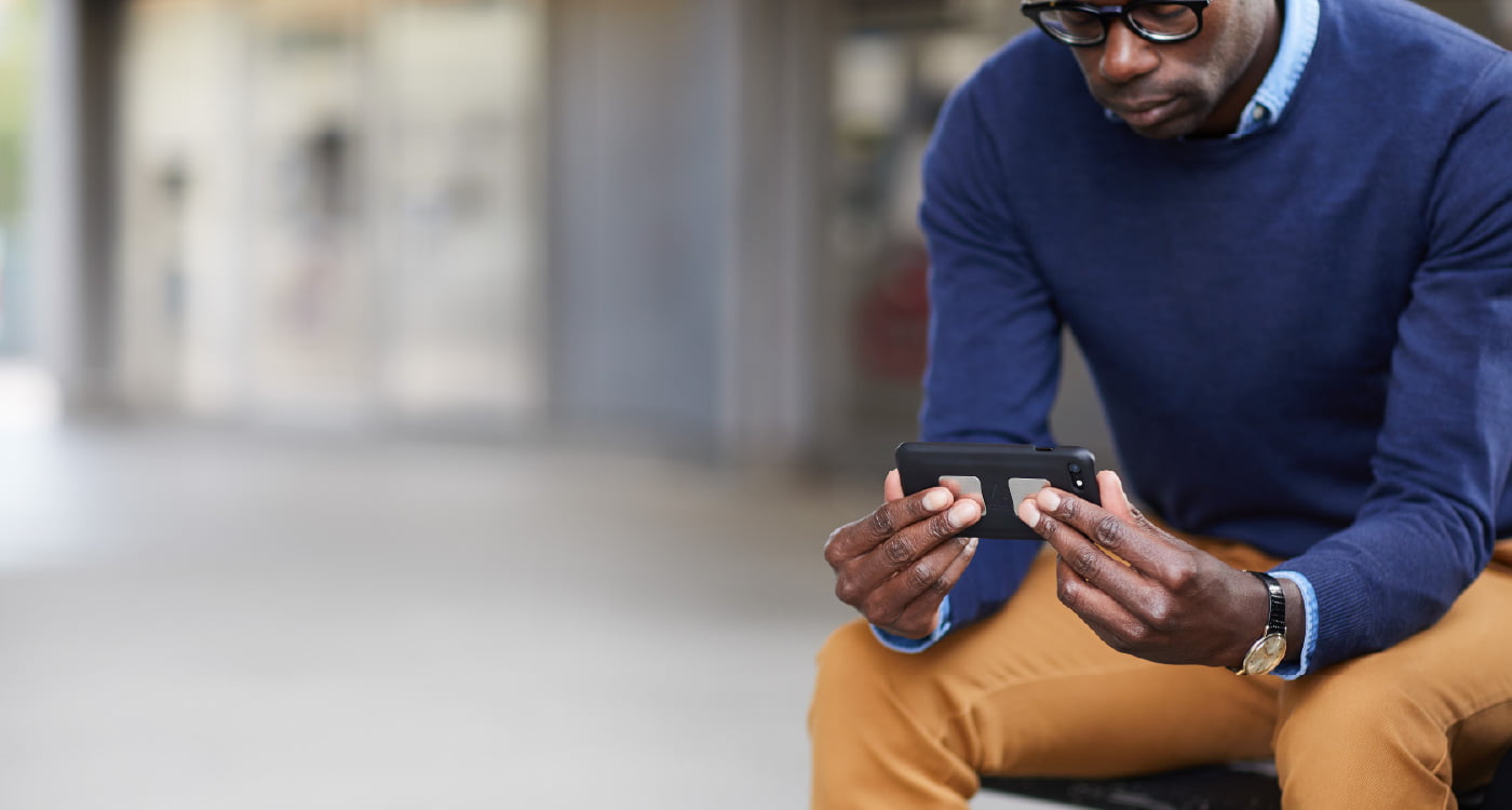 a man sitting on a bench holding his phone with KardiaMobile attached